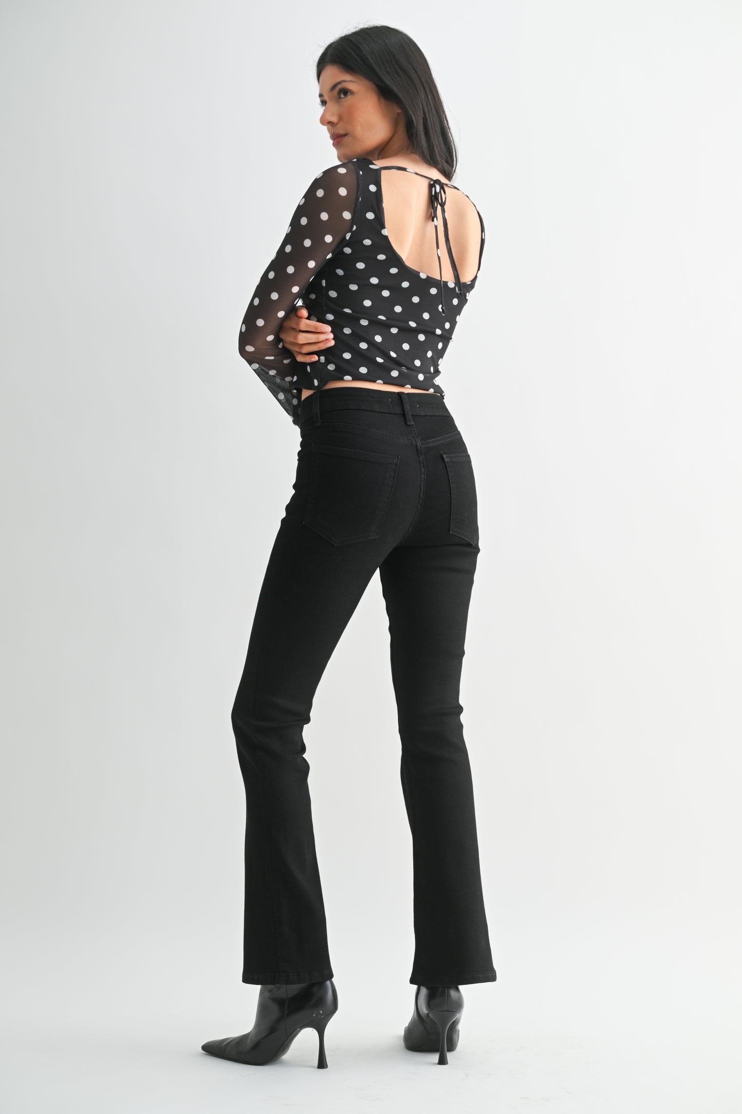Woman wearing a black polka dot top and black pants on a white background