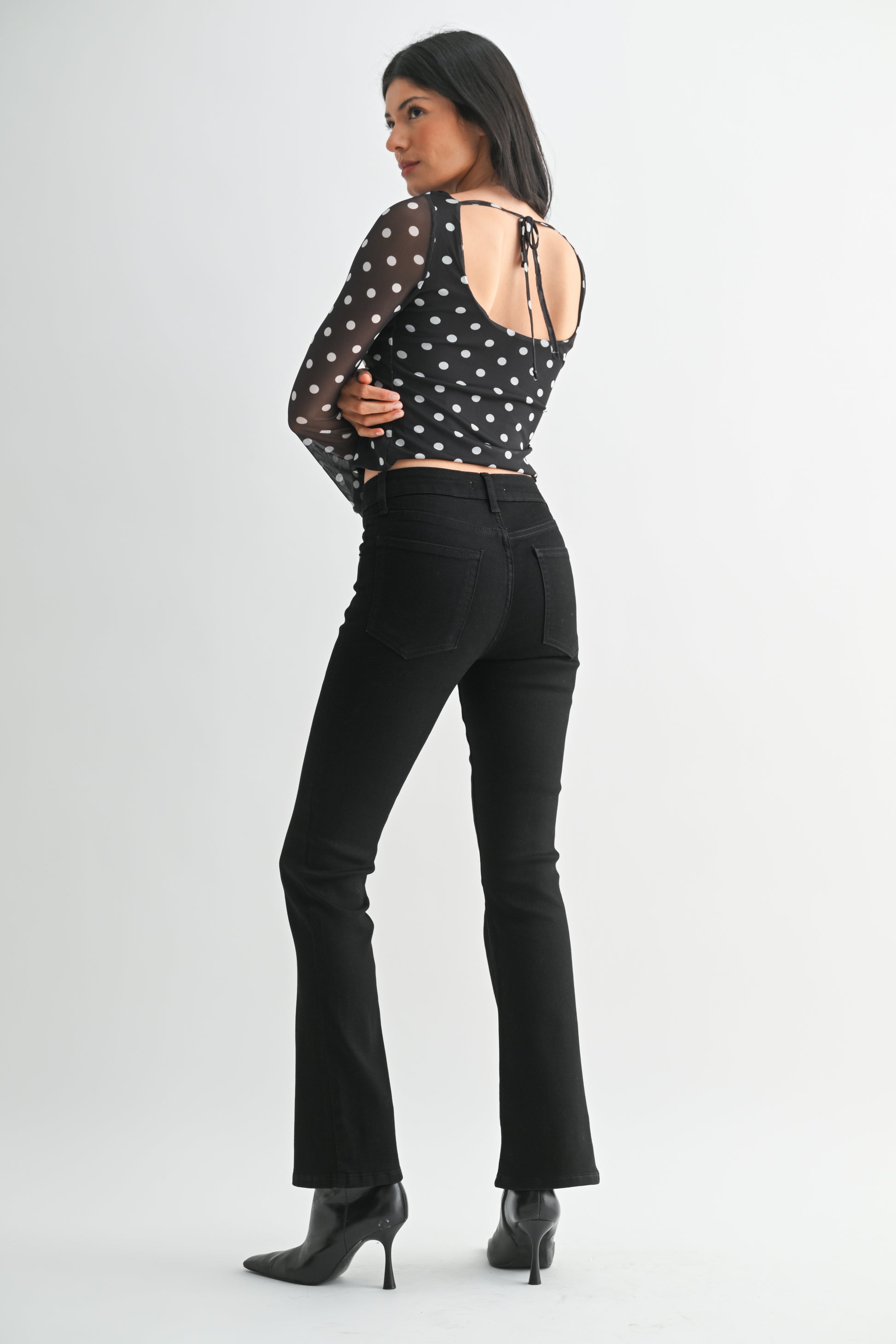 Woman wearing a black polka dot top and black pants on a white background