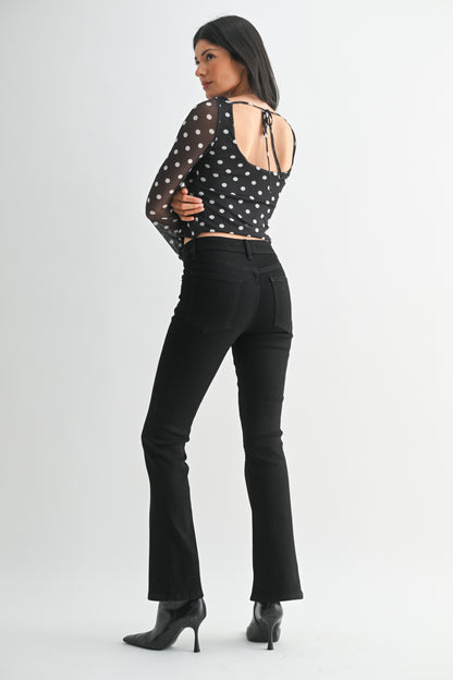 Woman wearing a black polka dot top and black pants on a white background