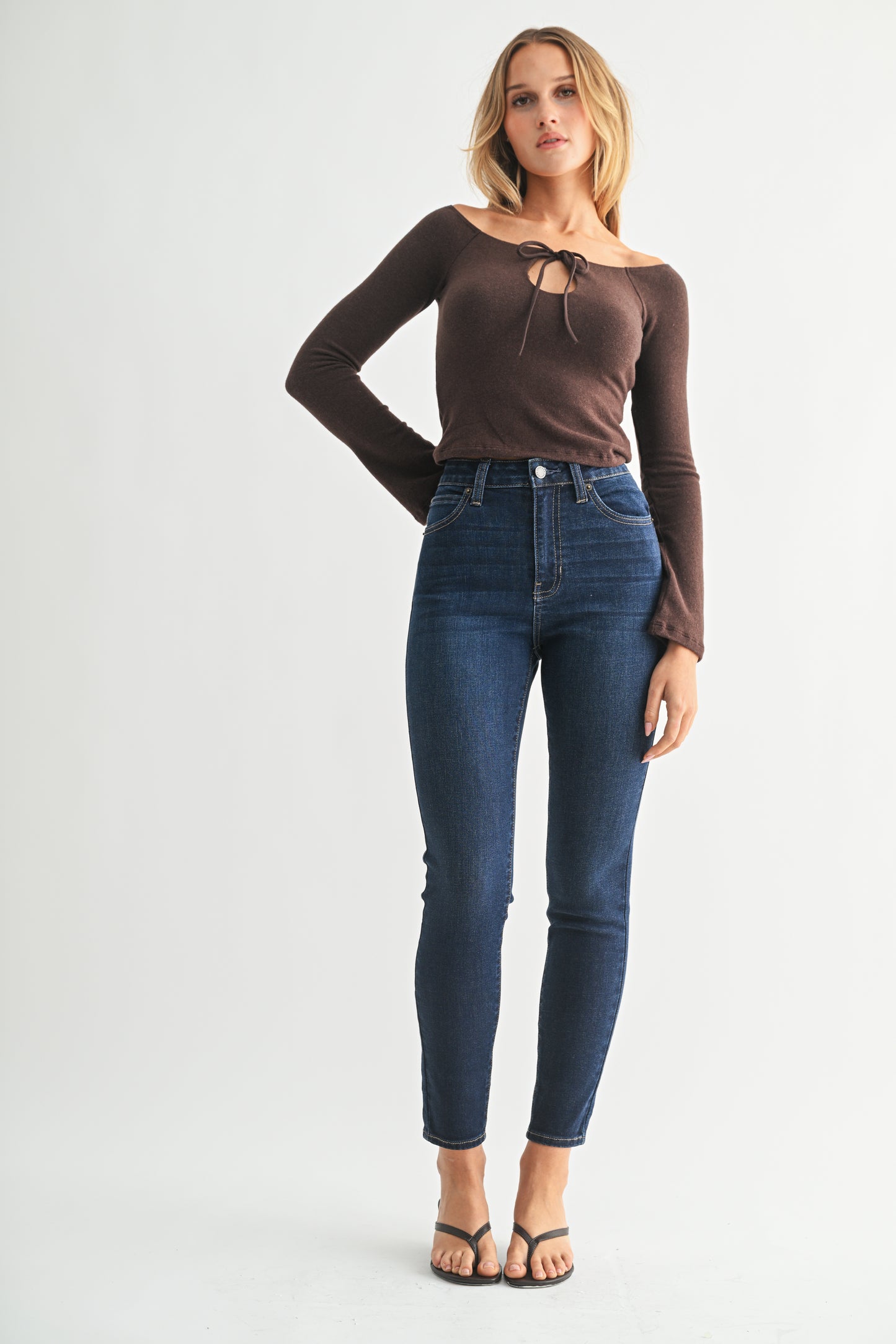 Woman wearing a brown long-sleeve top and blue jeans on a white background