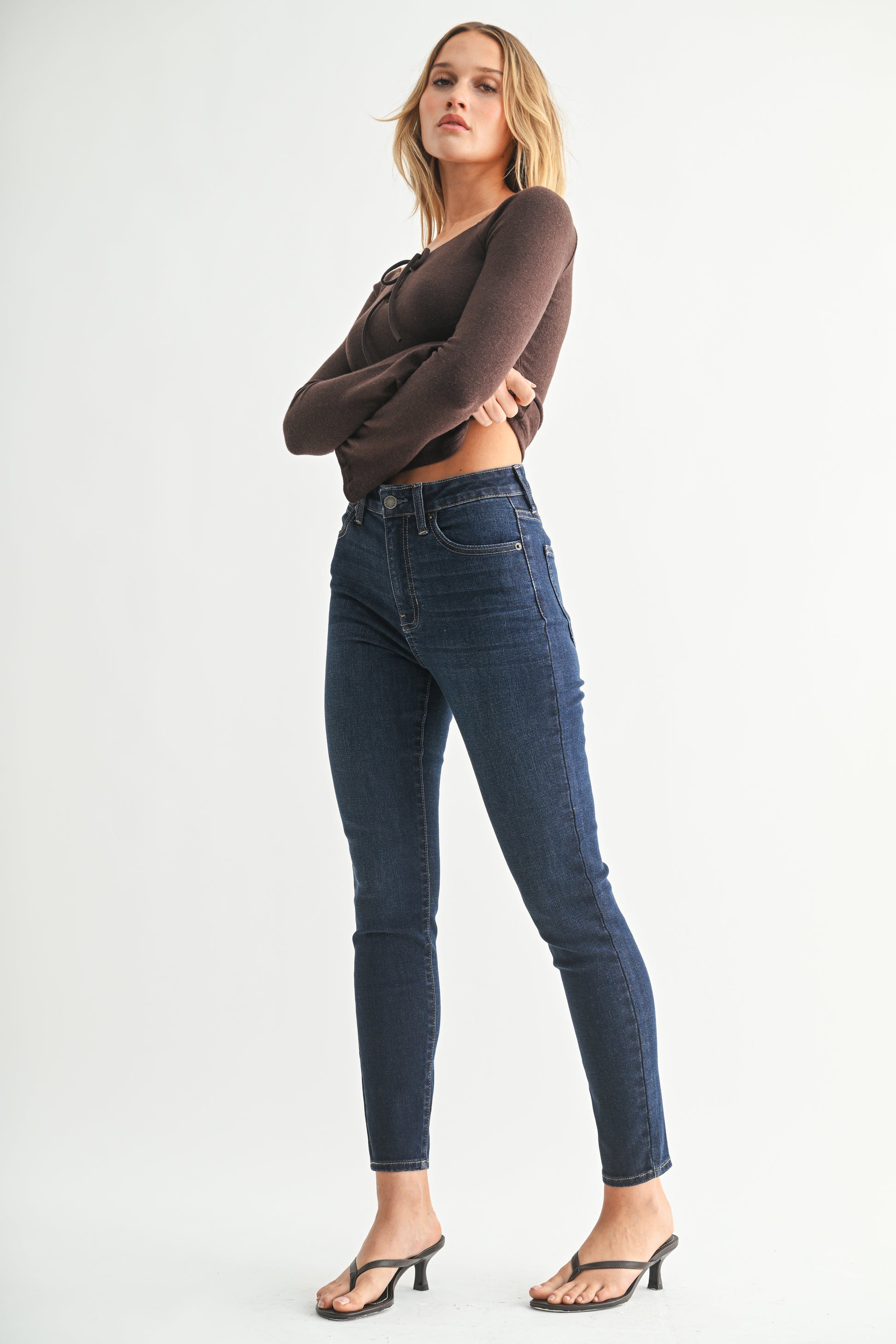 Woman wearing blue jeans and a brown top on a white background