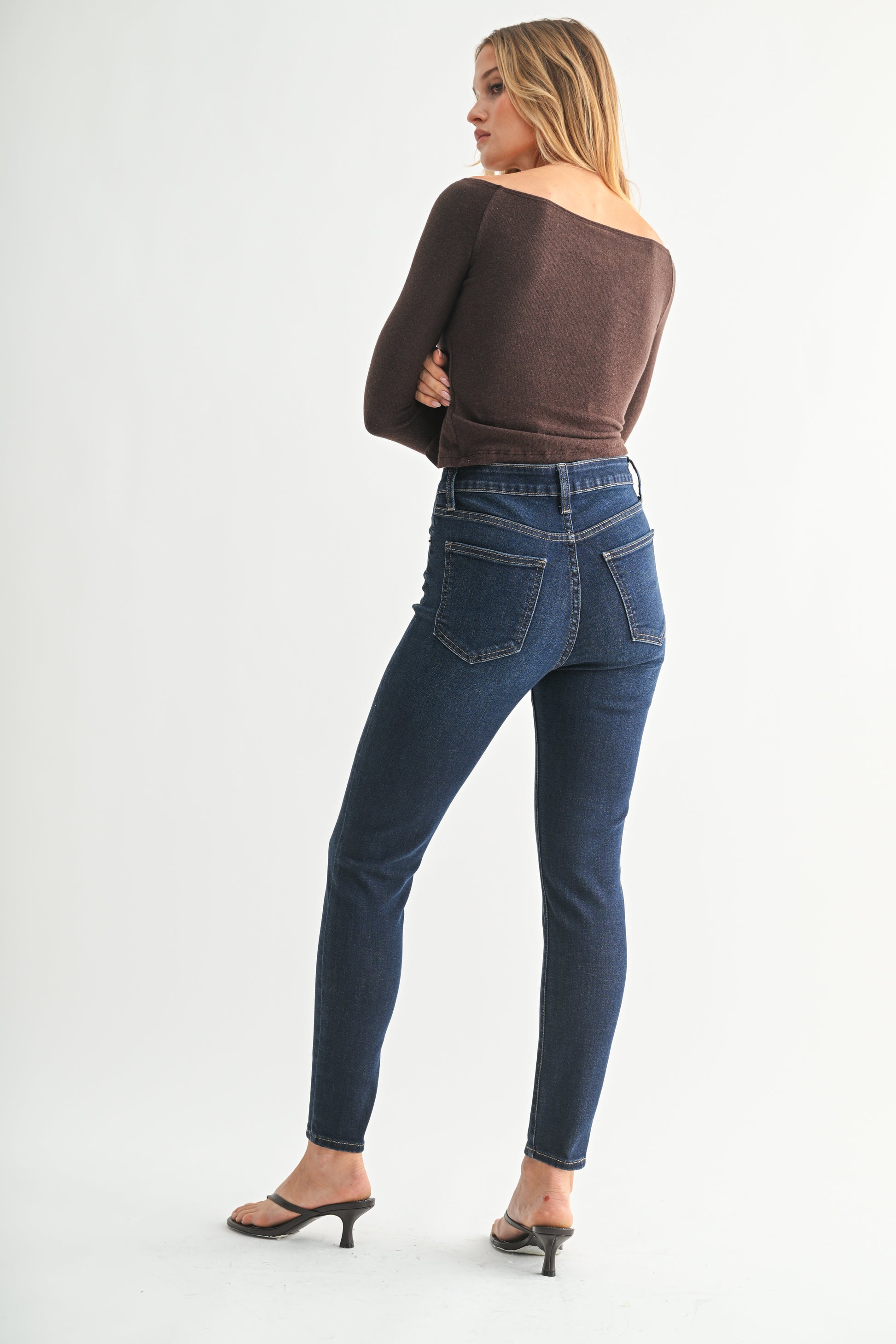 Woman wearing blue jeans and a brown top on a white background