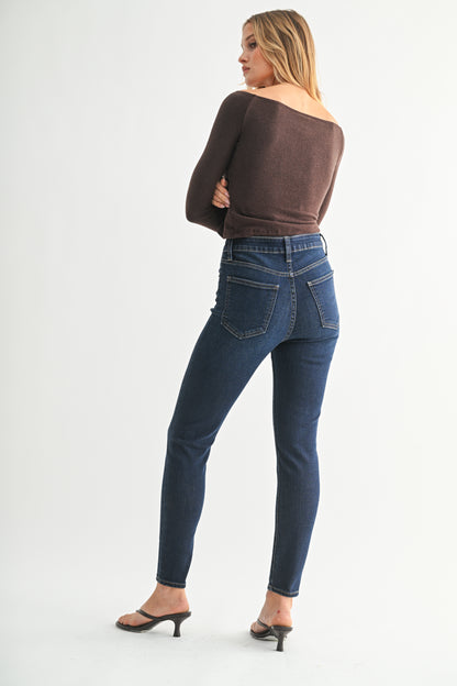 Woman wearing blue jeans and a brown top on a white background