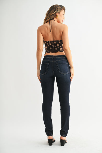 Woman wearing dark blue jeans and a black patterned top on a white background