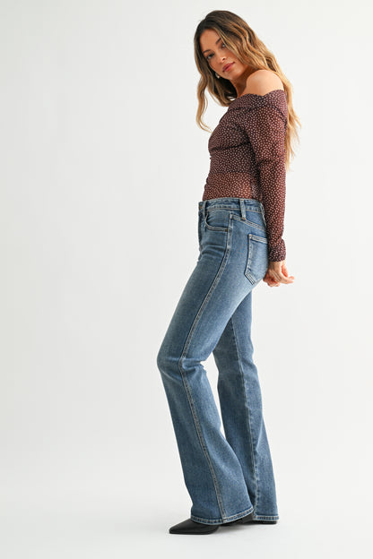 Woman wearing a patterned top and blue jeans on a white background