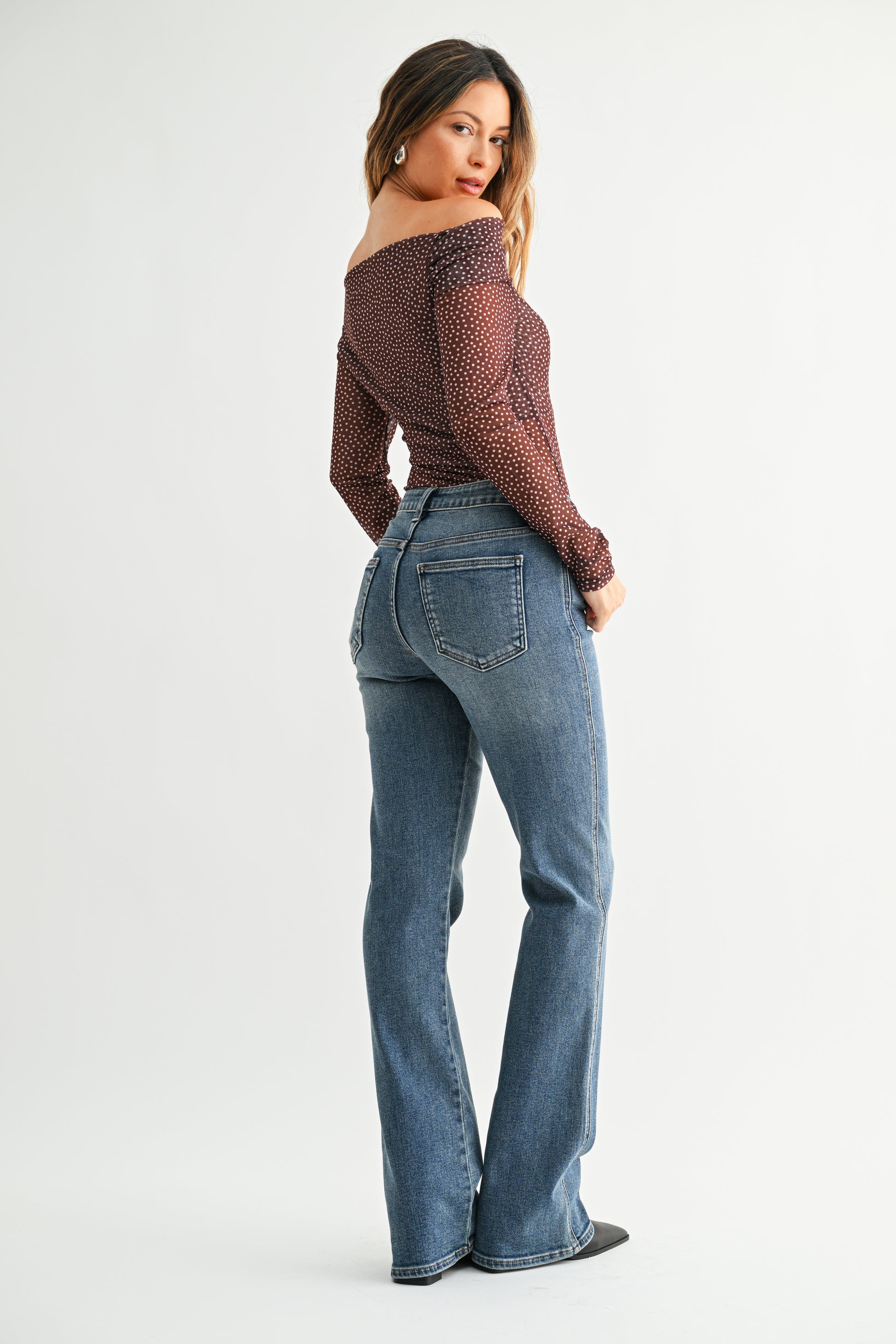 Woman wearing a patterned off-shoulder top and blue jeans on a white background
