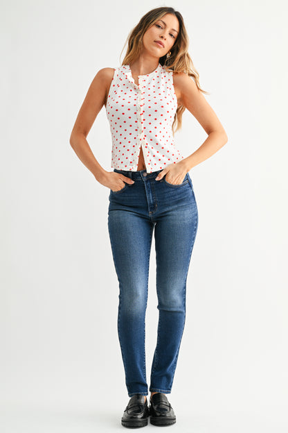Woman wearing a white sleeveless top with red patterns and blue jeans on a white background