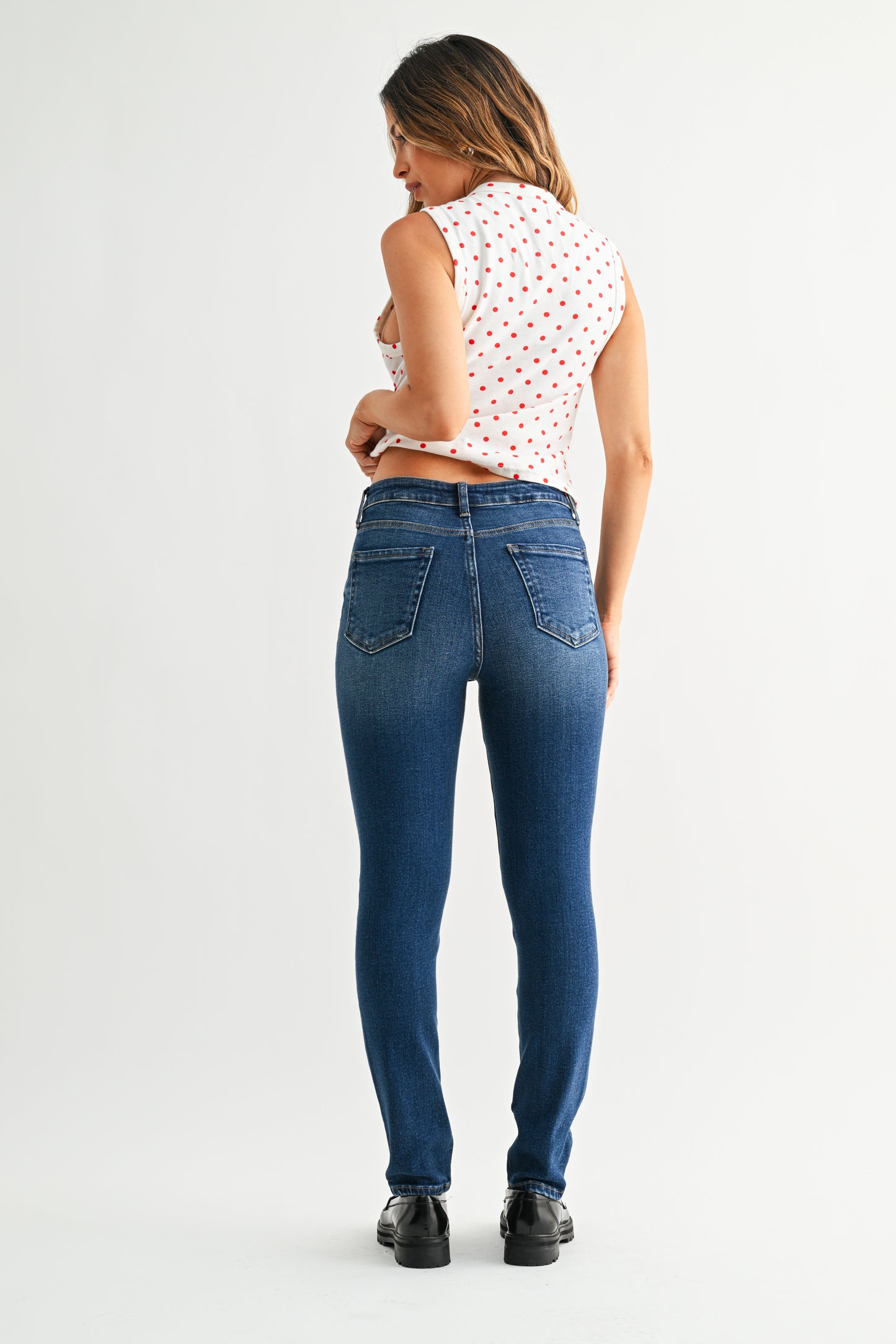 Woman wearing blue jeans and a white sleeveless top with red patterns on a white background