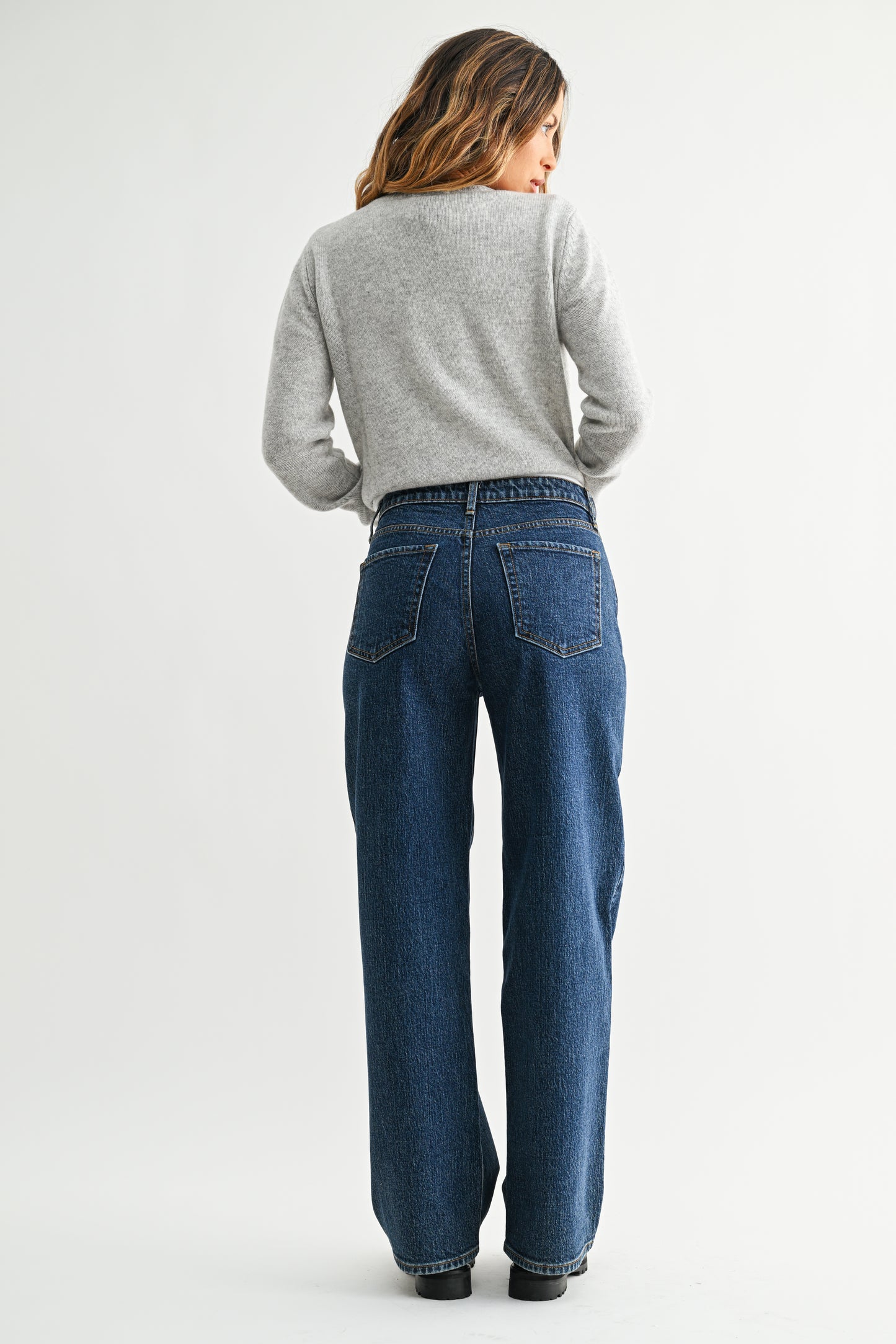 Person wearing blue jeans and a gray sweater on a white background