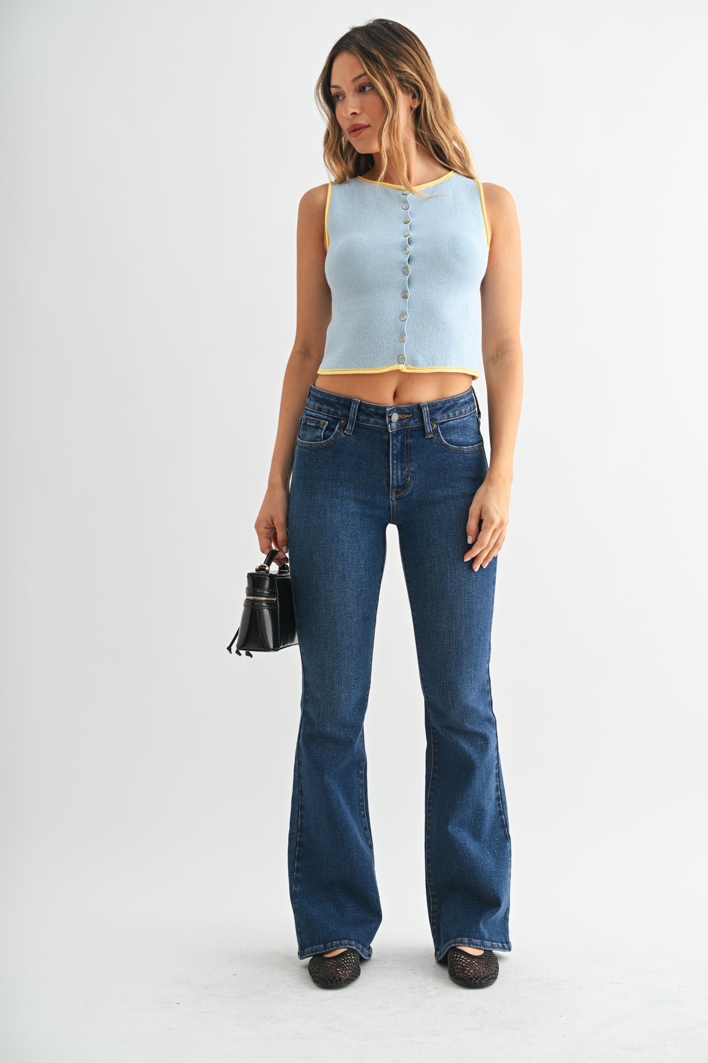 Woman wearing a light blue sleeveless top and dark blue jeans on a white background