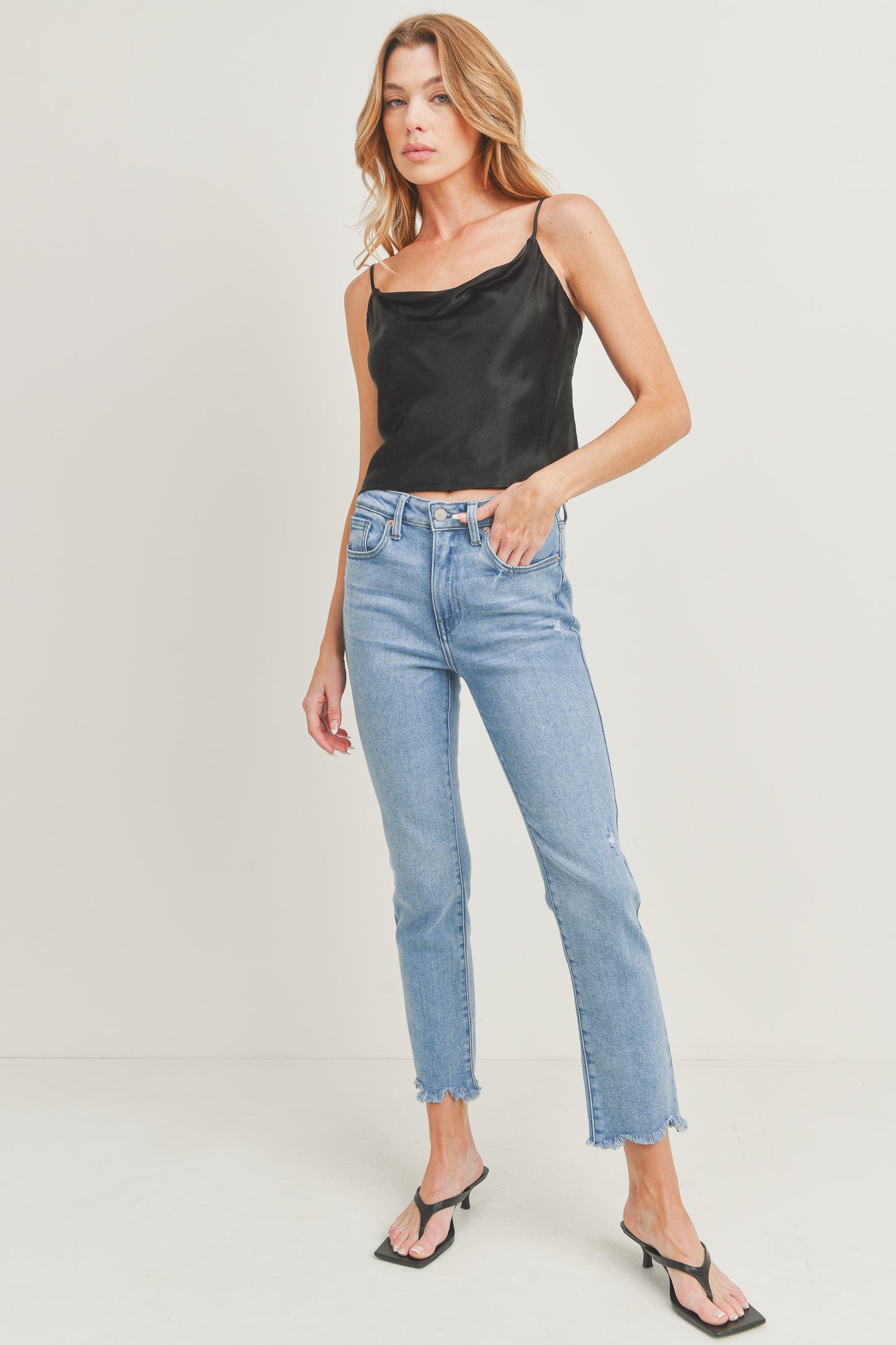 Woman wearing a black tank top and light blue jeans on a white background