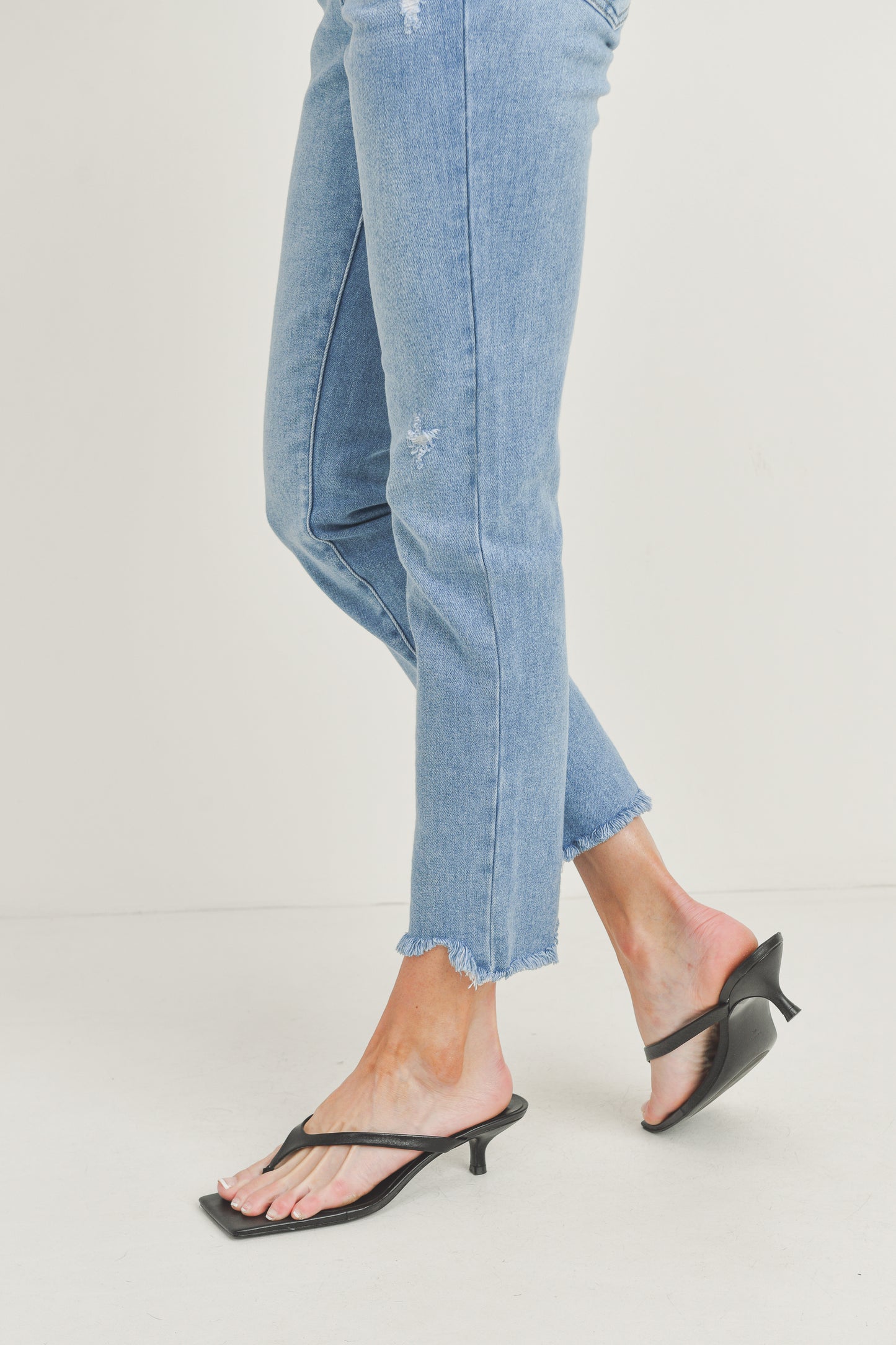 Light blue jeans worn with black kitten heel sandals on a light gray background
