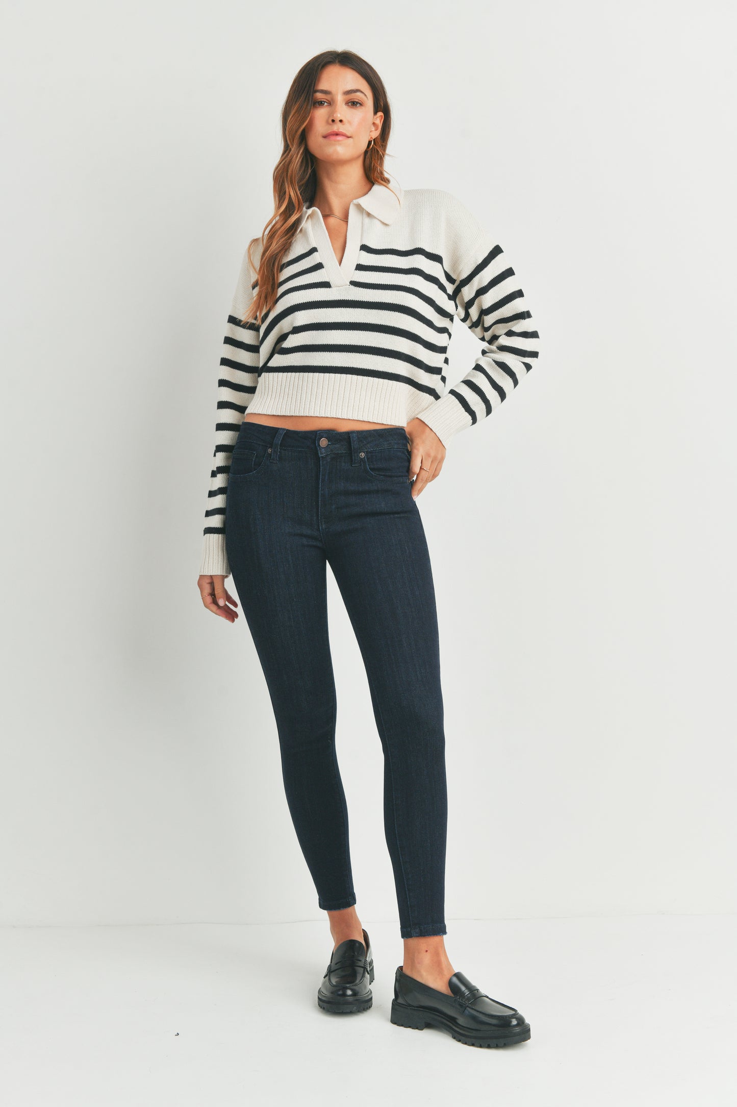 Woman wearing a black and white striped sweater and dark jeans on a white background