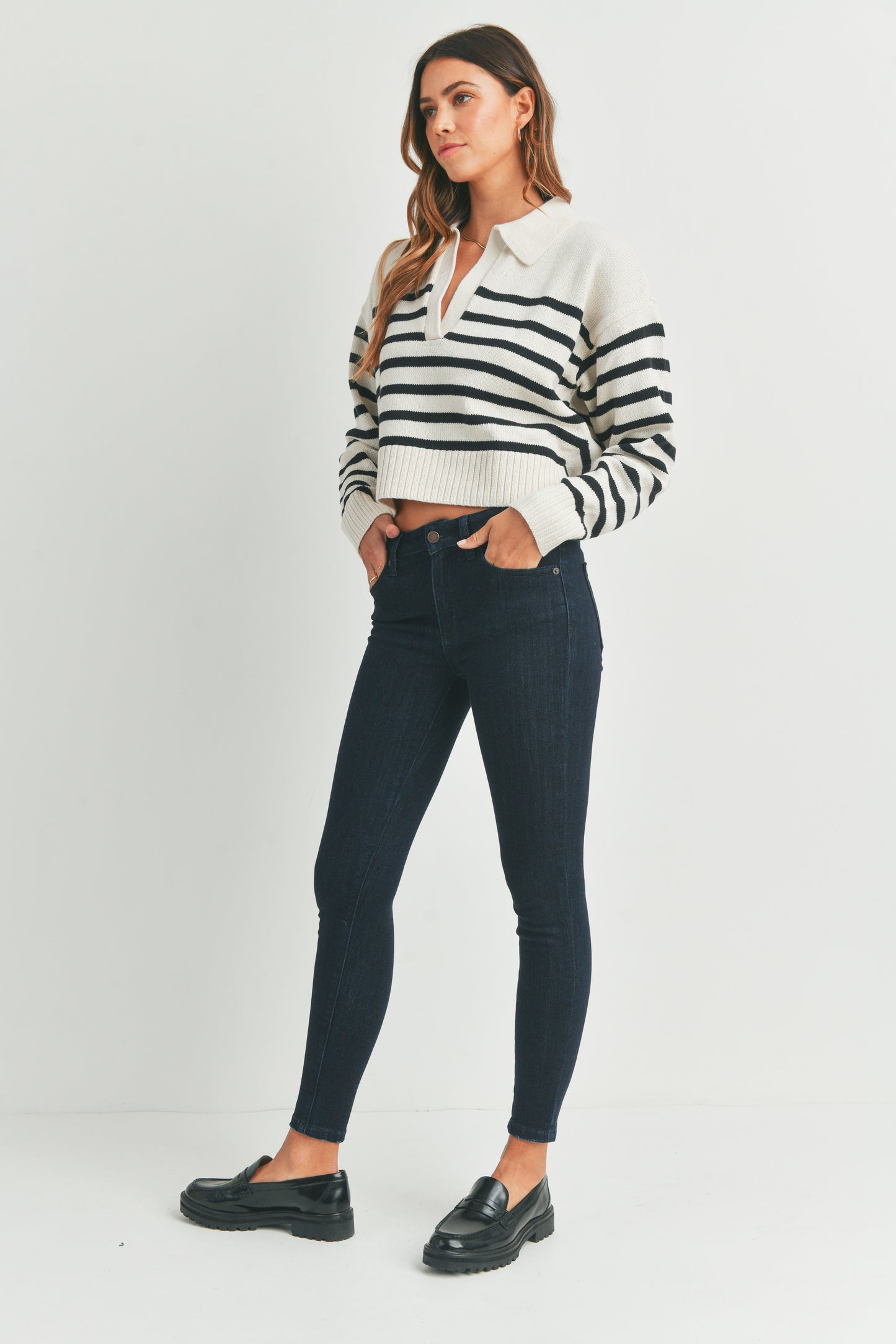 Woman wearing a black and white striped shirt with dark jeans on a white background