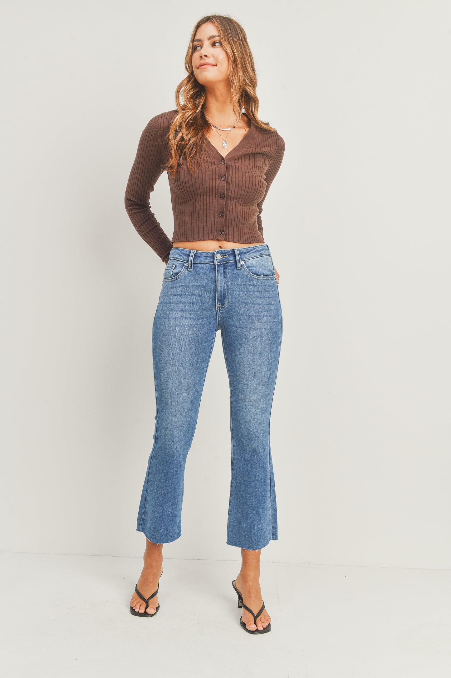 Woman wearing a brown ribbed sweater and blue jeans on a white background