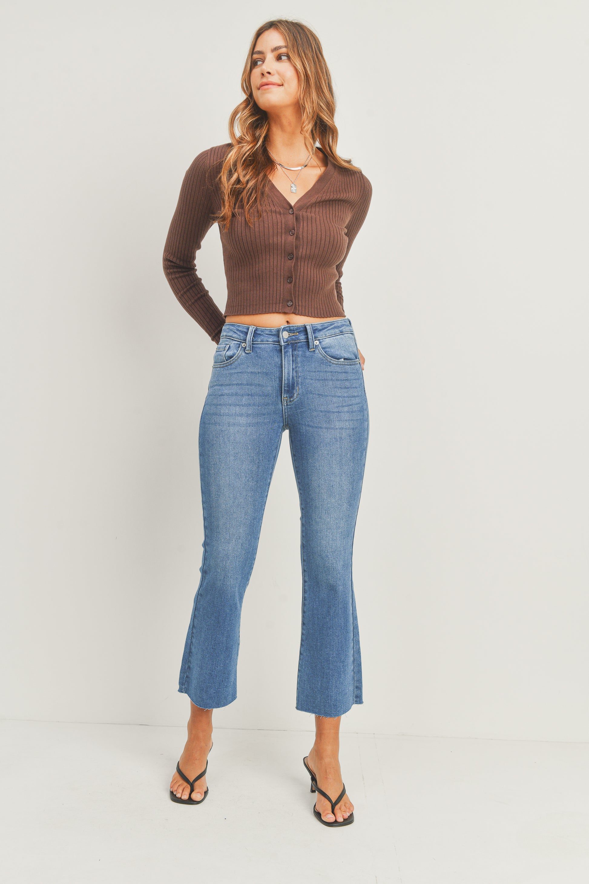 Woman wearing a brown ribbed sweater and blue jeans on a white background