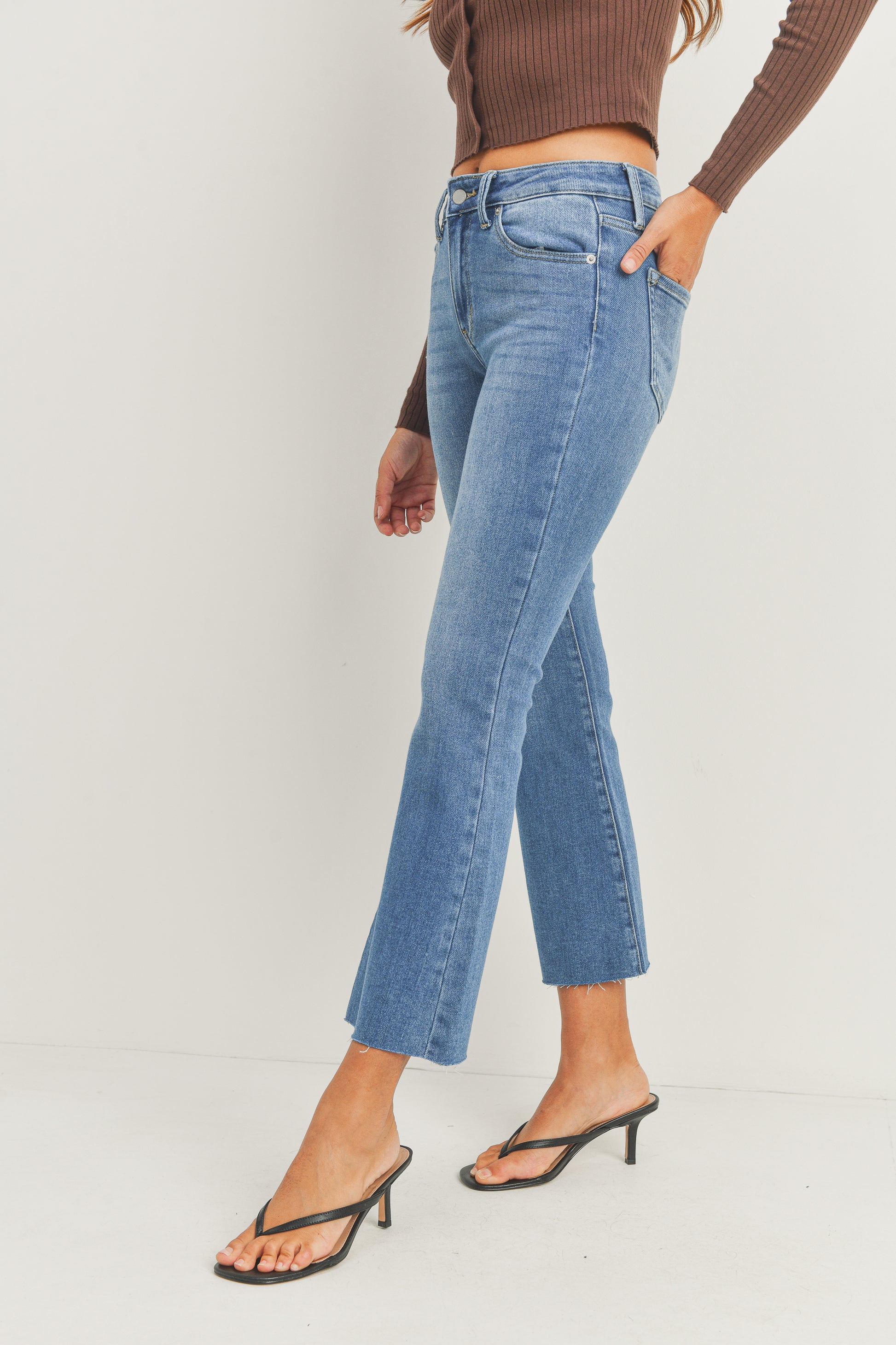 Person wearing blue jeans and a brown top on a white background