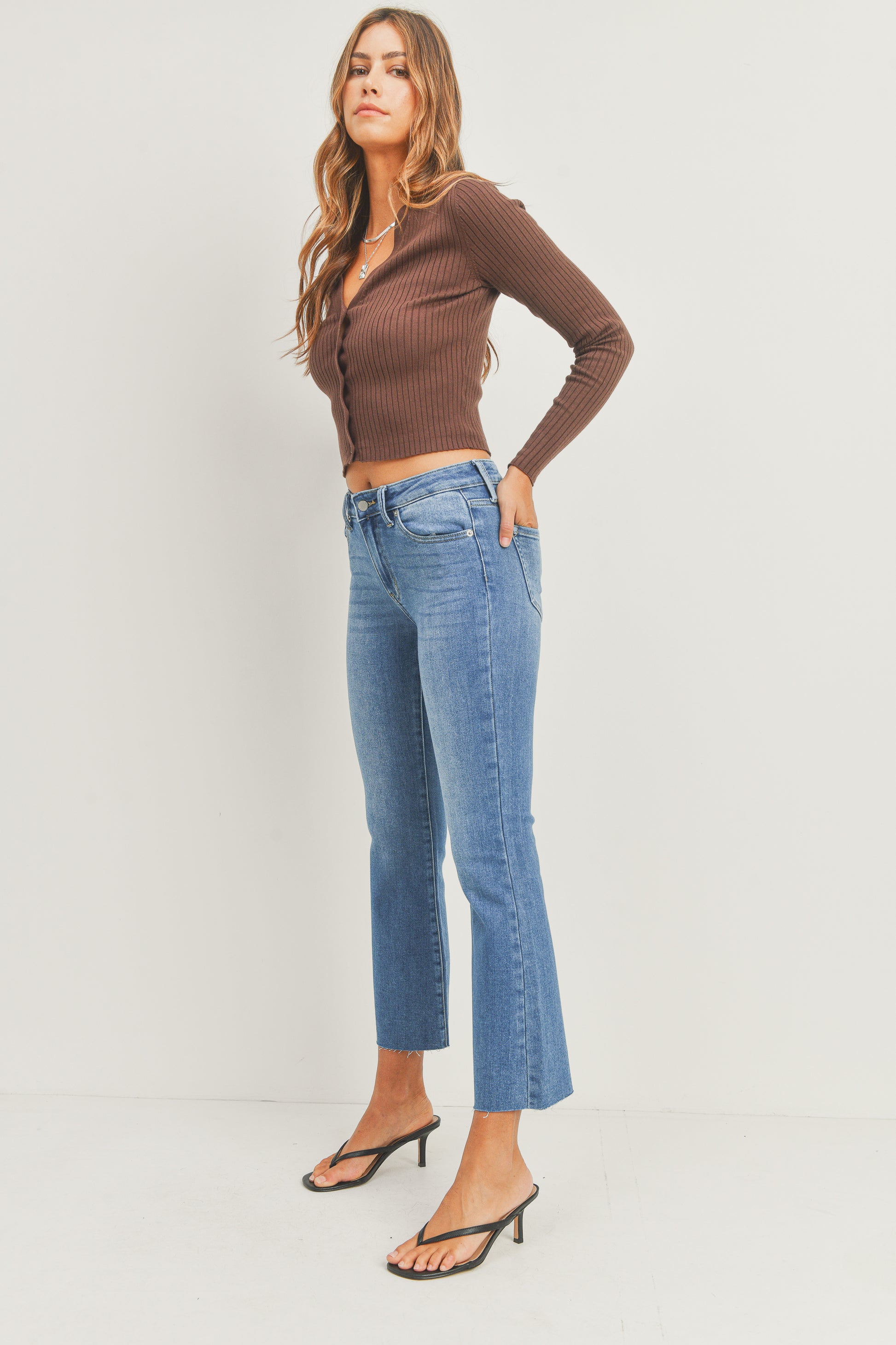 Woman wearing a brown long-sleeve top and blue jeans on a white background