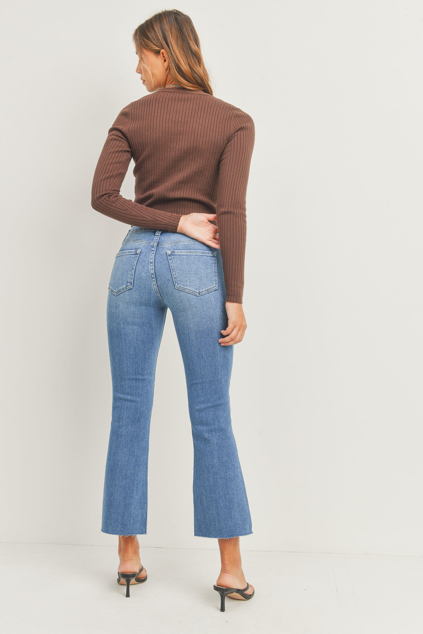 Woman wearing a brown ribbed sweater and blue jeans on a plain background