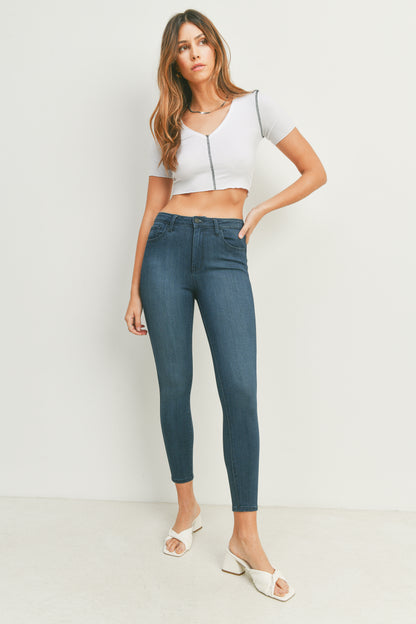 Woman wearing a white crop top and blue jeans against a plain background