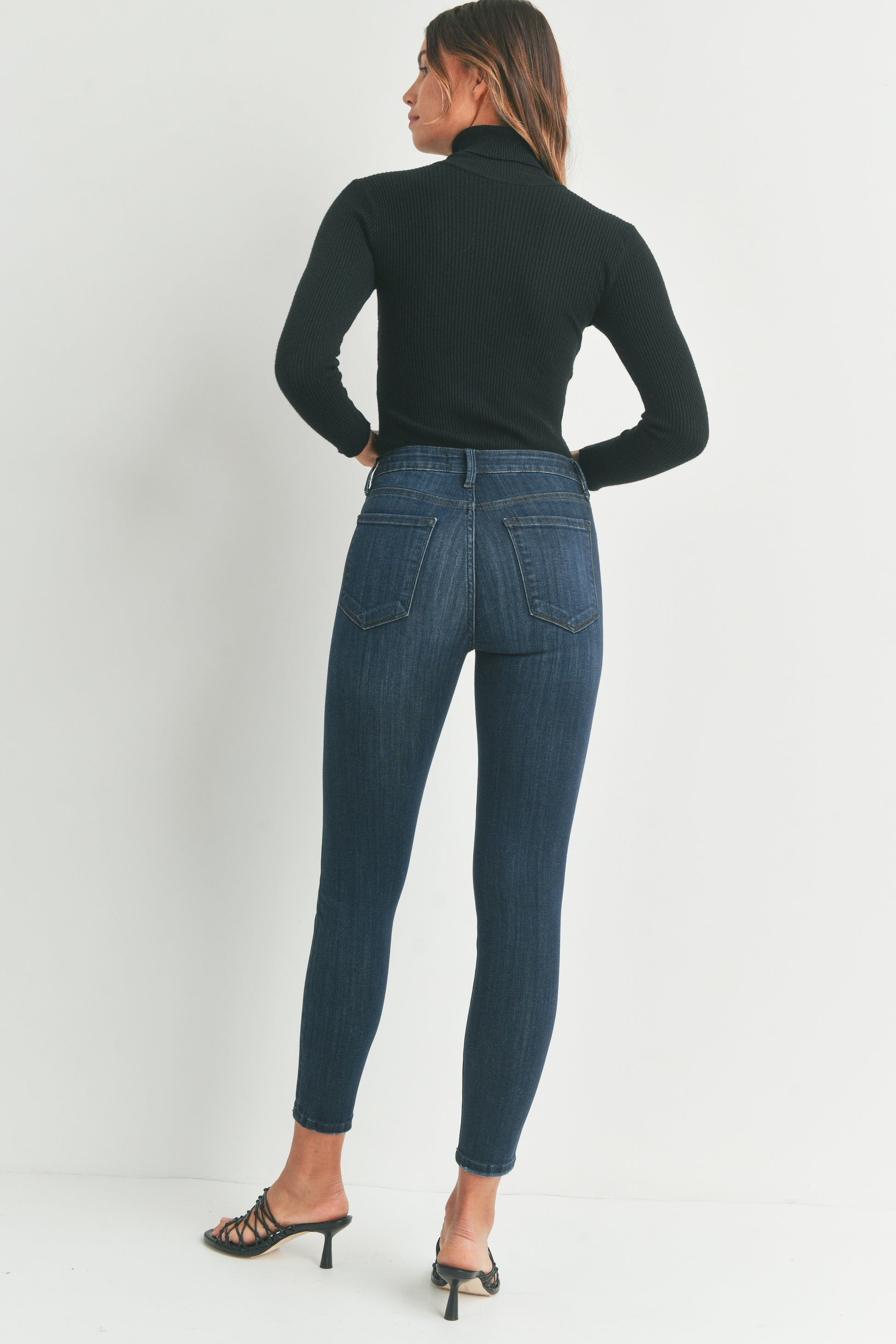 Woman wearing blue jeans and a black turtleneck on a white background