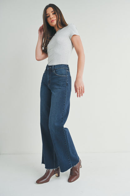 Woman wearing blue jeans and a white top on a plain background